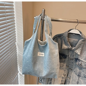 Detail view of light blue denim tote bag with white bow prints and woven label design