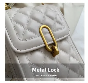 Close-up of matte gold U-shaped metal lock on a quilted white crossbody leather bag