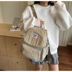Dettaglio dello zaino pieghettato kaki con tasche laterali a coulisse e patch logo