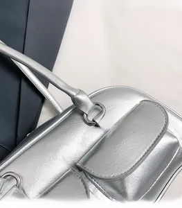 Détail d'un sac bandoulière argenté métallisé avec deux poches à rabat et fine lanière