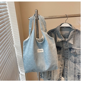 Detail of light blue denim tote bag with white bow patterns and branded fabric label