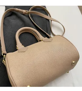 Detail view of beige woven barrel bag with leather handles and gold metal hardware