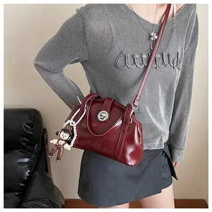 Détail d'un sac à main bordeaux en cuir verni avec fermoir métal et pendentif mignon