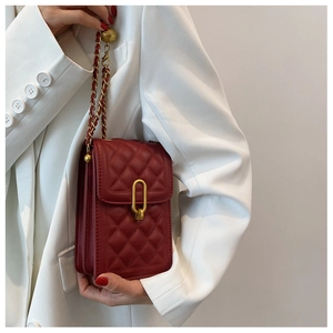 Detail of red quilted crossbody bag with gold chain and U-shaped clasp on white blazer