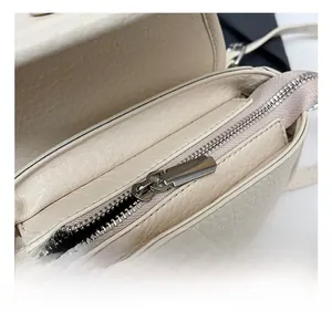 Detail of silver metal zipper and textured white litchi leather on a crossbody bag