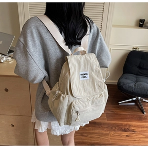 Dettaglio dello zaino beige in tela con tasca frontale a zip ed etichetta del marchio
