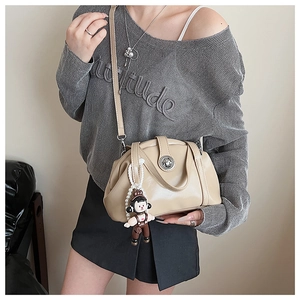 Gros plan d'un sac bandoulière plissé beige avec fermoir argenté et breloque en perles