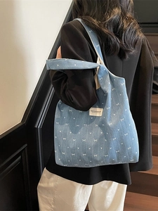 Blue denim tote bag with white bow prints and wide shoulder strap shown on a model
