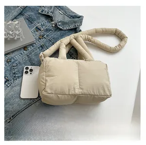 Détail d'un sac cabas beige matelassé avec bandoulière rembourrée sur table blanche