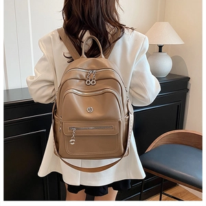 Rear view of model wearing a brown PU leather backpack with silver zippers and multi-pockets