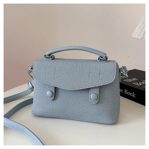 Detail of light blue textured fabric shoulder bag with dual buckle closure and leather trim