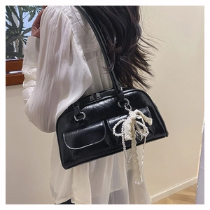 Détail d'un sac à bandoulière noir brillant avec poches frontales et pendentif nœud perlé