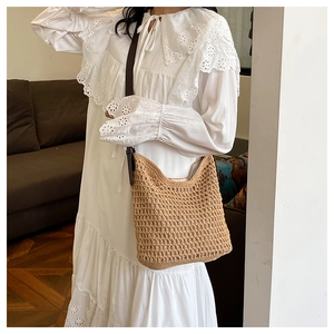 Détail d'un sac seau en paille tressée marron avec motif ajouré et bandoulière en cuir
