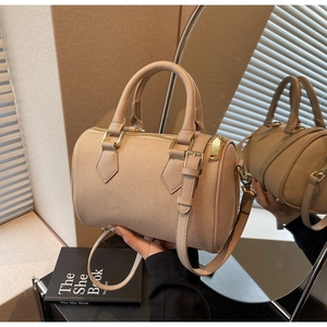 Close-up of beige canvas and leather barrel bag featuring golden hardware and top handles