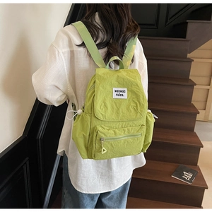 Dettaglio dello zaino in tela verde con patta e patch bianca sulla tasca anteriore