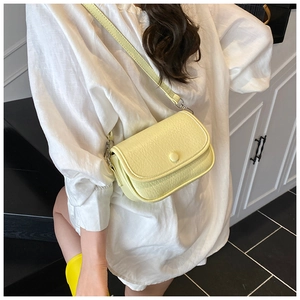 Detail view of a pale yellow faux leather saddle bag worn with a white casual shirt