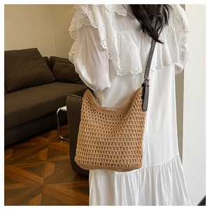 Détail du sac seau en paille tissée avec bandoulière en cuir brun sur robe blanche
