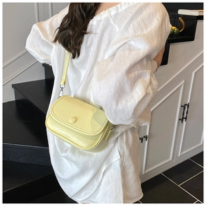 Detail view of the pale yellow crossbody bag with smooth pebble texture and round buckle