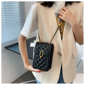 Close-up of a black quilted mobile phone bag with golden chain strap on a model