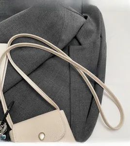 Détail d'un mini sac bandoulière beige en cuir grainé avec une fine bandoulière cylindrique