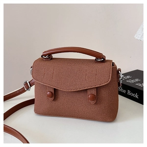 Detail of brown textured fabric crossbody bag with leather handle and retro flap design