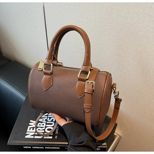 Detail of a brown cylindrical Boston bag with leather trim and gold metal zippers