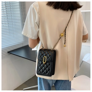 Detail of black quilted leather bag featuring a gold ring clasp and gold ball chain strap