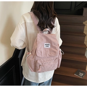 Dettaglio di uno zaino in tela rosa con etichetta indossato da modella su scale