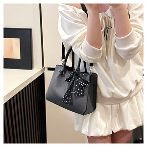 Détail d'un sac à main trapèze noir avec ferrures argentées et foulard en soie à pois
