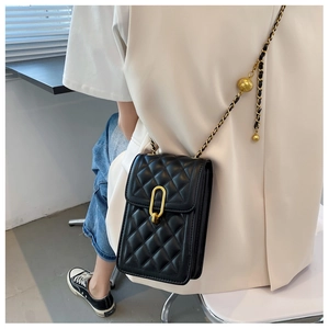 Detail of black quilted leather crossbody bag with gold buckle and chain strap on model