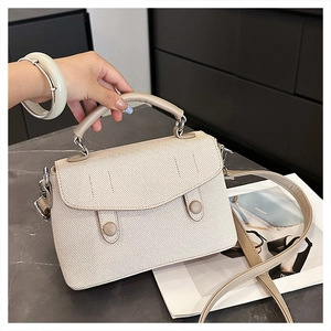 Detail of beige textured flap handbag with dual round buckles and silver hardware