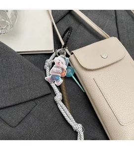 Détail du sac à bandoulière beige texturé pour téléphone avec sangle tissée et pendentifs