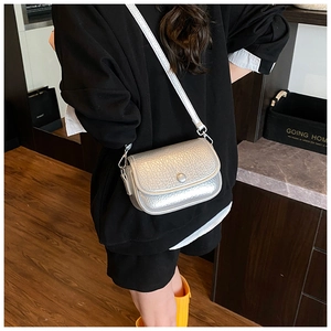 Detail view of a silver crossbody square bag with metallic texture on a model shoulder