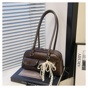 Détail du sac bowling marron brillant avec nœud en dentelle et poches sur des livres