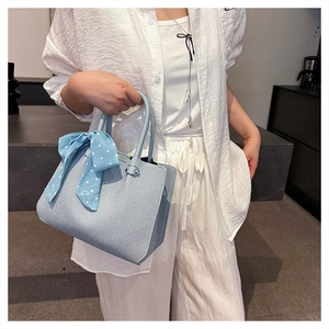 Détail du sac à main bleu clair avec foulard à pois, porté par un mannequin en blanc