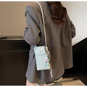 Petit sac bandoulière en cuir bleu clair à motif litchi porté sur un blazer gris
