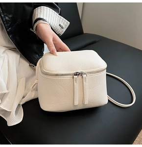 Detail einer weißen Mini-Umhängetasche aus Lychee-Leder mit silbernen Reißverschlüssen
