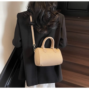 Detailed view of a beige Boston handbag with golden hardware on wooden stairs
