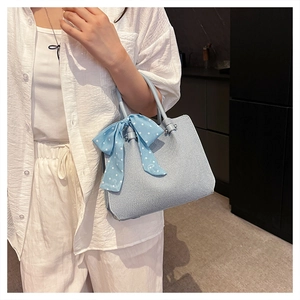 Détail du sac seau bleu clair avec ruban à pois porté par un mannequin en décor moderne