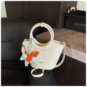 Detail of cream crocodile embossed handbag with a blue pegasus charm on a black leather chair