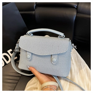 Detail of light blue twill fabric handbag with silver hardware and sturdy round handle