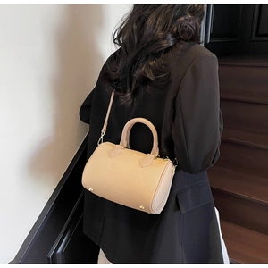 Close-up of beige cylinder Boston bag with gold hardware and textured leather finish