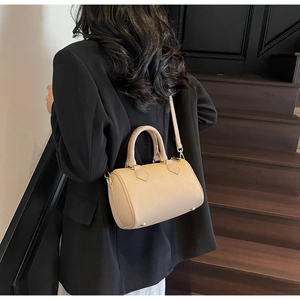 Detail view of beige Boston bag with gold hardware and removable shoulder strap worn cross-body