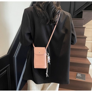 Sac bandoulière rose texture litchi avec breloque à glands porté par un mannequin en tailleur noir