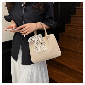 Détail d'un sac seau tissé beige avec poignée en cuir marron et ruban à pois élégant