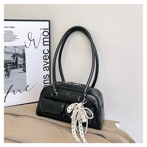 Détail du sac bowling noir avec pendentif nœud en dentelle et chaîne de perles sur tissu