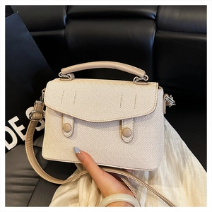 Detail view of beige textured crossbody bag featuring silver hardware and top handle strap