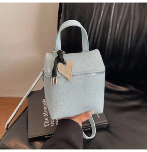 Dettaglio borsa quadrata in pelle azzurra con motivo litchi, zip e ciondolo a cuore