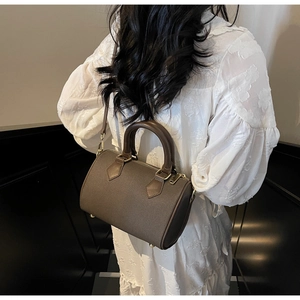 Brown canvas barrel bag worn over the shoulder with a white dress and leather strap