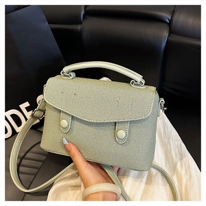 Close-up of light green woven fabric texture and round buckle details on stylish crossbody bag